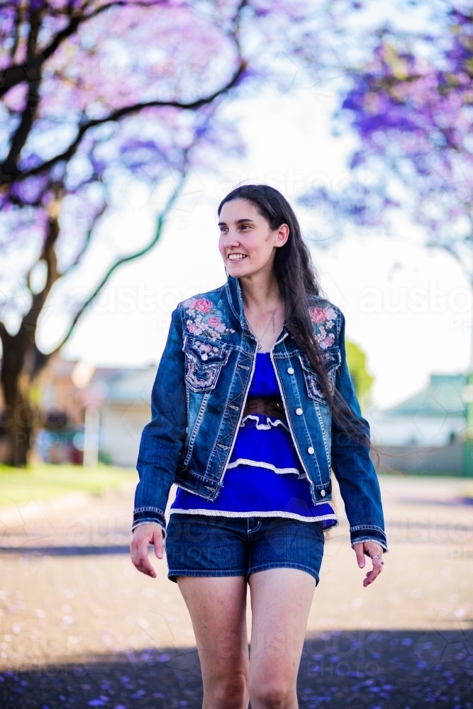 Woman in blue walking along road lined with flowering trees - Rawcliffe street, Singleton in spring - Australian Stock Image