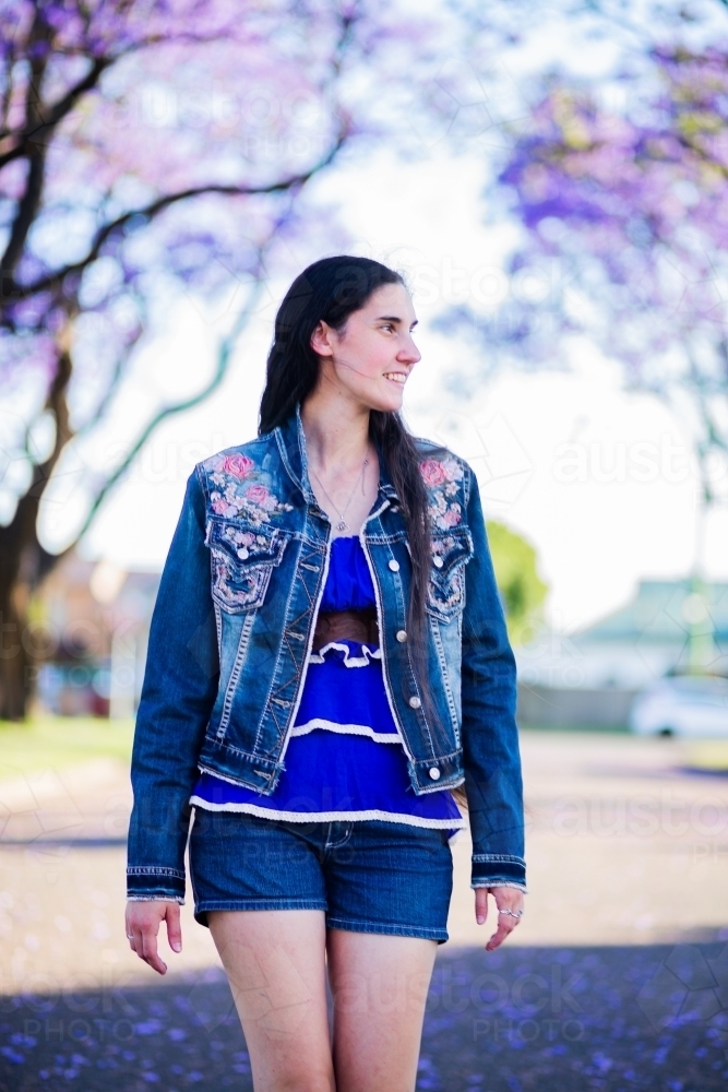 Woman in blue walking along road lined with flowering trees - Rawcliffe street, Singleton in spring - Australian Stock Image