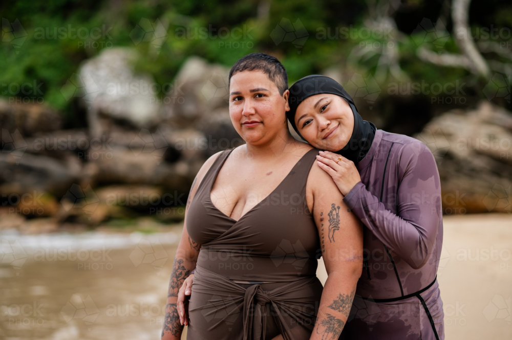 Woman in burkini resting her head on her friends shoulder on the beach - Australian Stock Image