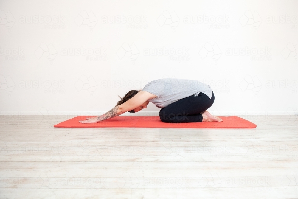 woman in child's pose doing yoga on mat in studio - Australian Stock Image
