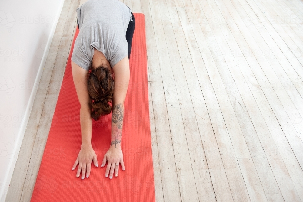 woman in child's pose on red mat in studio - Australian Stock Image