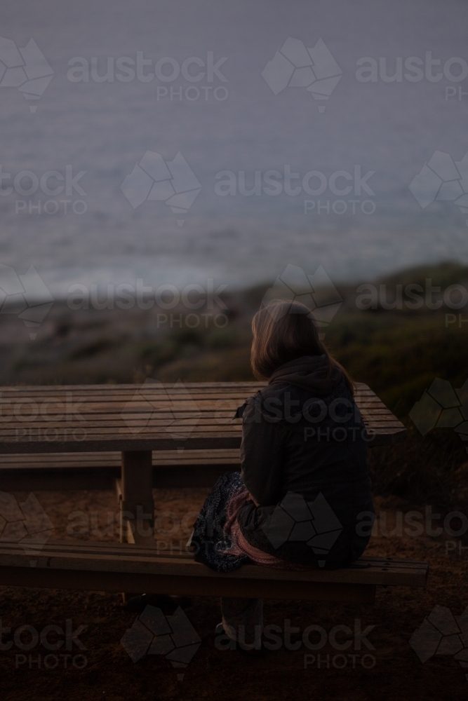 Woman in coat sitting looking out to sea in the dark - Australian Stock Image