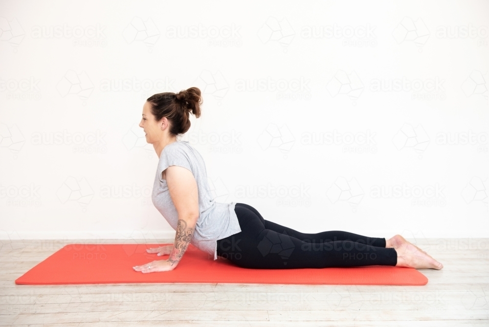 woman in cobra pose on red yoga mat in studio - Australian Stock Image