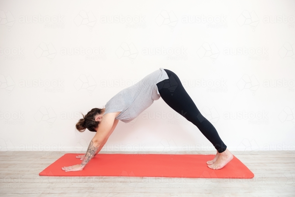 woman in downward dog yoga pose on red mat in studio - Australian Stock Image