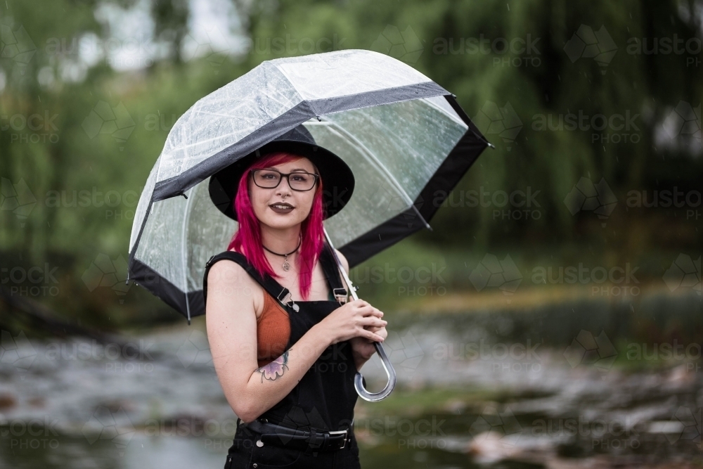 Woman in early 20s with coloured hair holding umbrella in rain - Australian Stock Image