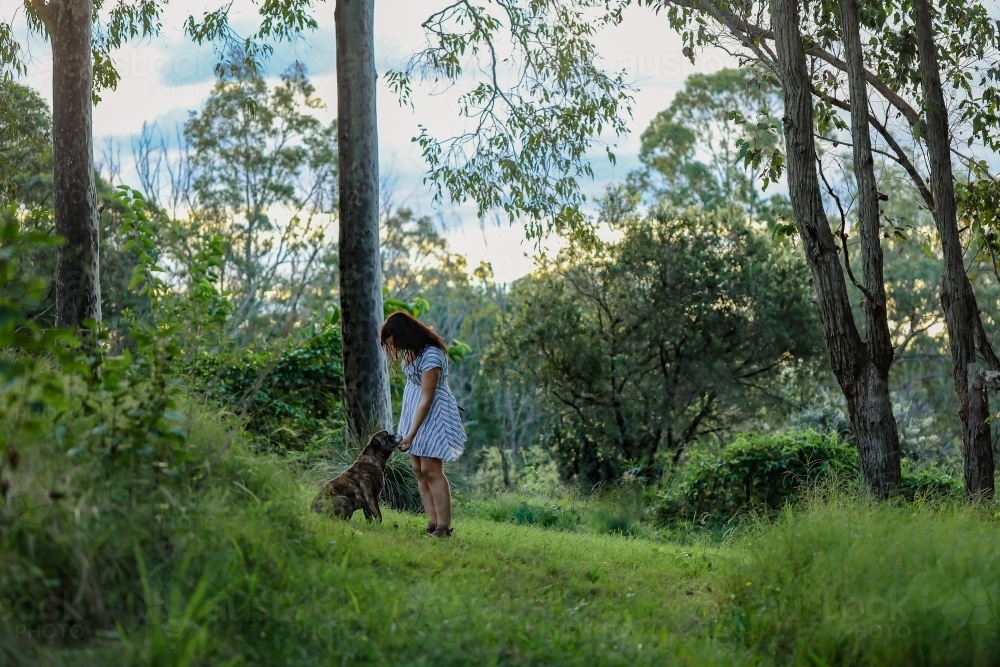 Woman in forest setting showing affection to pet dog - Australian Stock Image