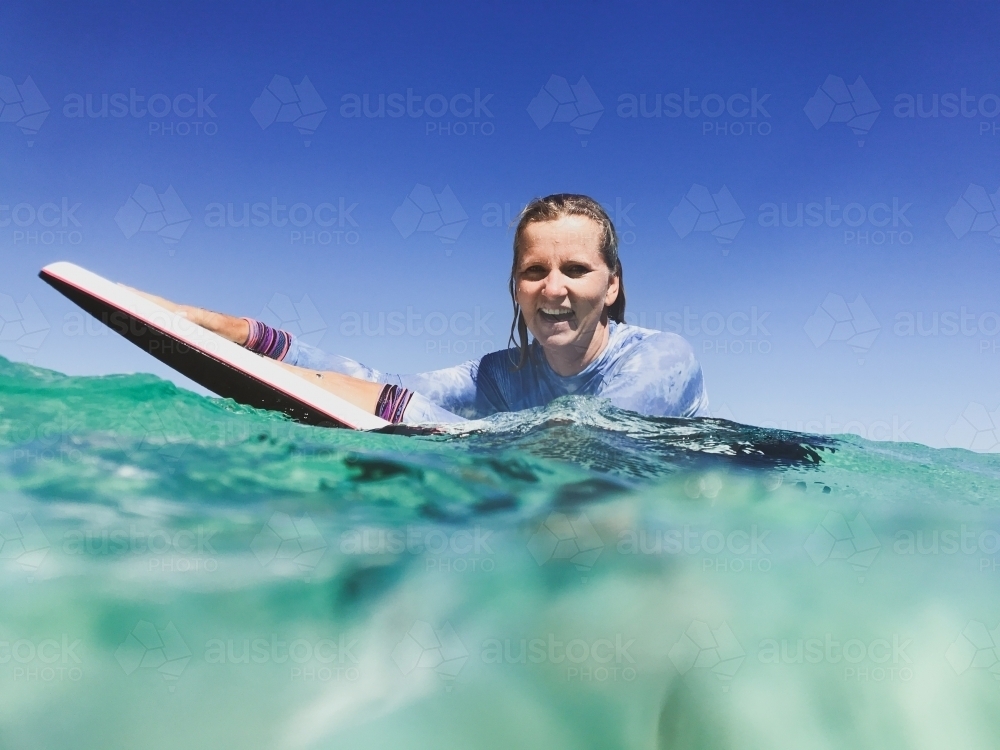 Woman in ocean with boogie board looking at camera smiling - Australian Stock Image