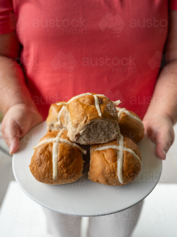 Woman in pink shirt holding white plate of hot cross buns - Australian Stock Image