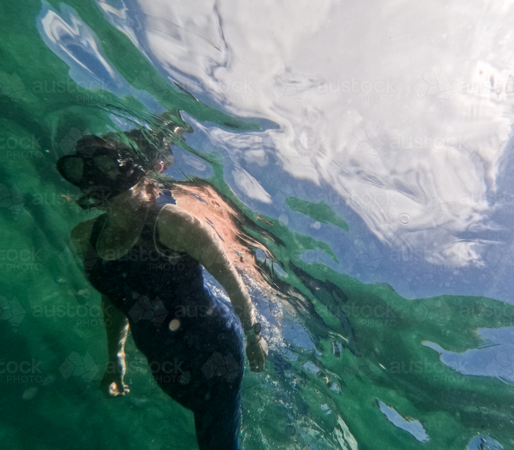 Woman in wetsuit snorkelling in ocean with cloudy sky visible - Australian Stock Image