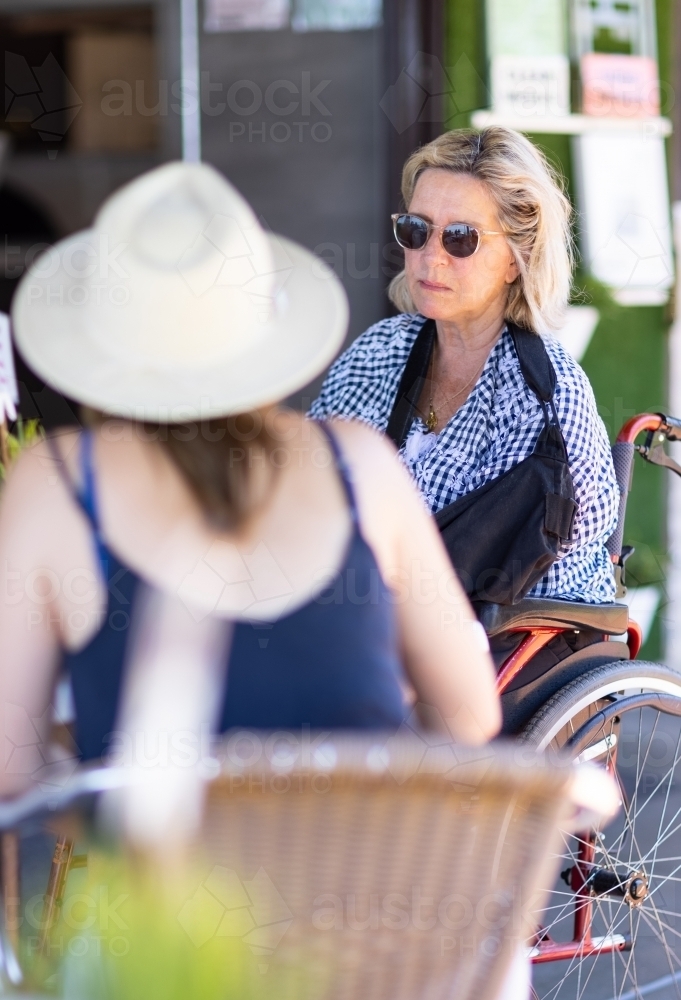 woman in wheelchair chatting with blurred woman sitting in foreground - Australian Stock Image