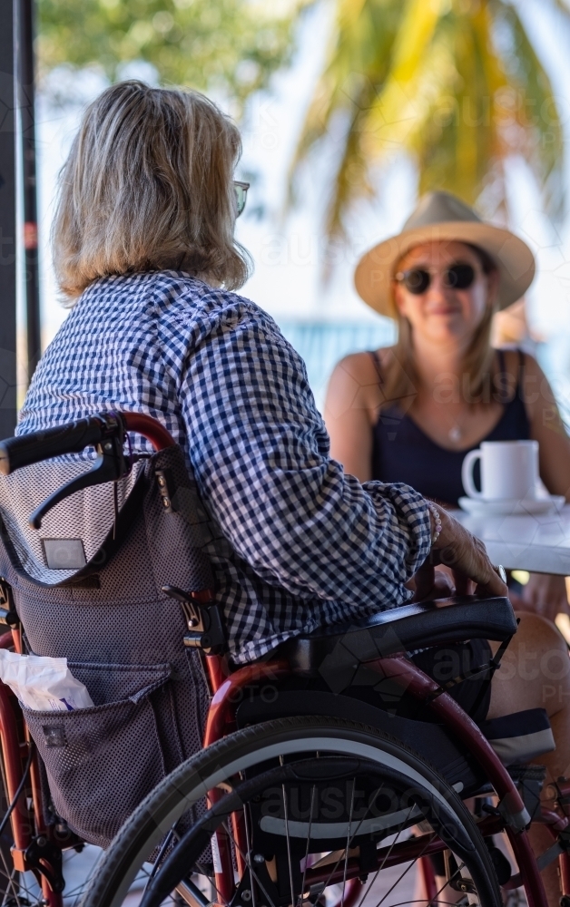 woman in wheelchair having cuppa with  younger woman near palm trees - Australian Stock Image