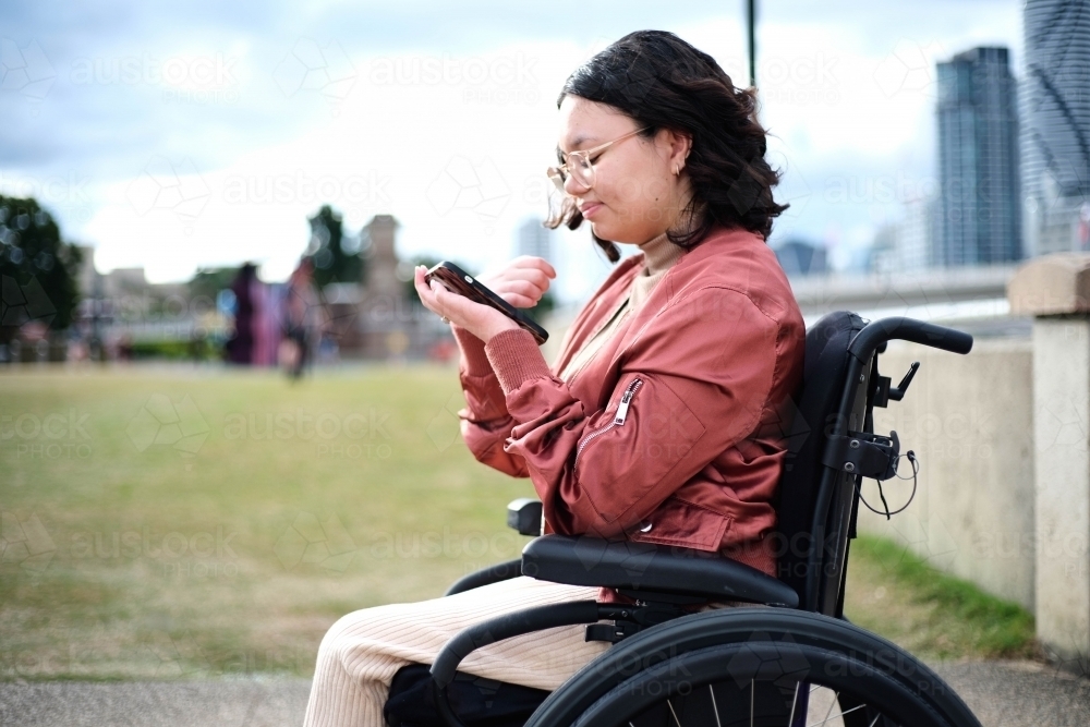Woman in wheelchair outside looking at her phone - Australian Stock Image