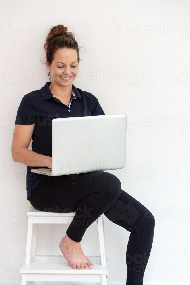 woman in workout gear working on laptop with smile - Australian Stock Image