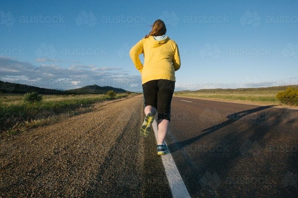 Woman jogging away on a remote country road - Australian Stock Image