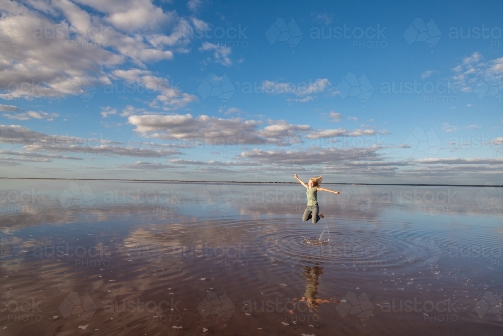 Woman jumping in the air over a salt lake. - Australian Stock Image