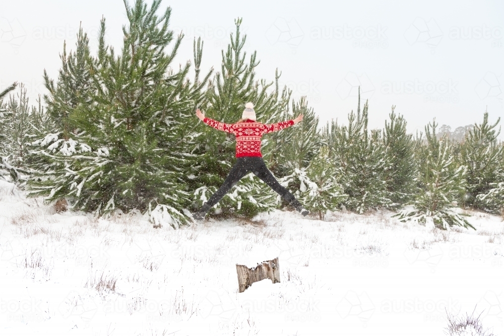Woman jumps high into the air on a snowy winter day - Australian Stock Image
