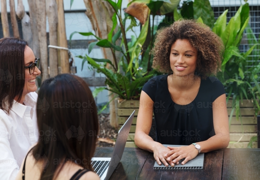 Woman laughing and working with colleagues at table outdoors - Australian Stock Image