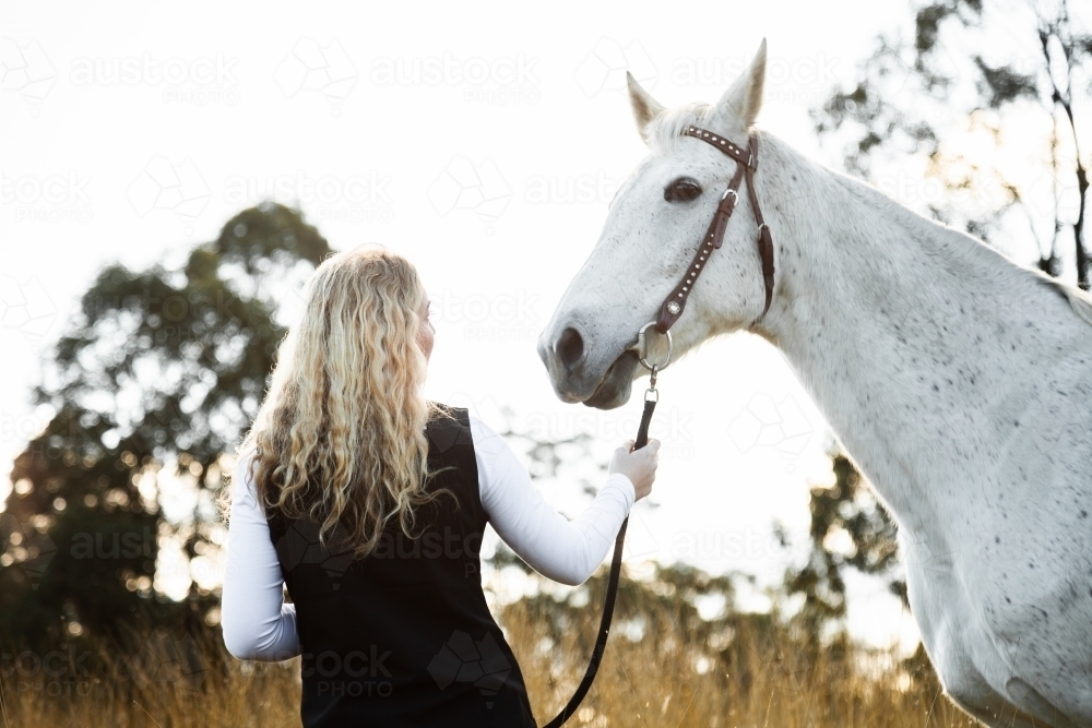 Woman leading her horse through the paddock of long grass - Australian Stock Image