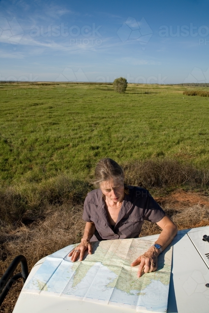 Woman leaning of the bonnet of her car in rural area, reading a map - Australian Stock Image
