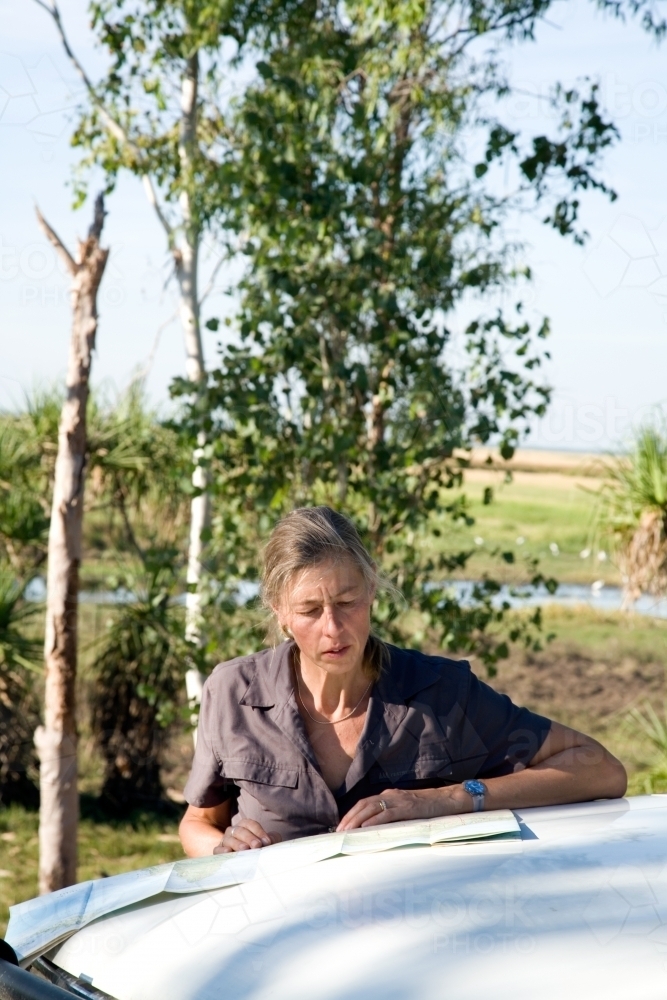 Woman leaning of the bonnet of her car in rural area, reading a map - Australian Stock Image