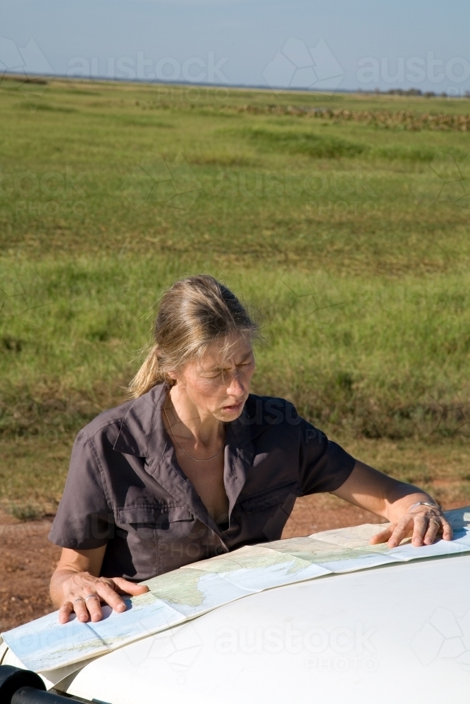 Woman leaning of the bonnet of her car in rural area, reading a map - Australian Stock Image