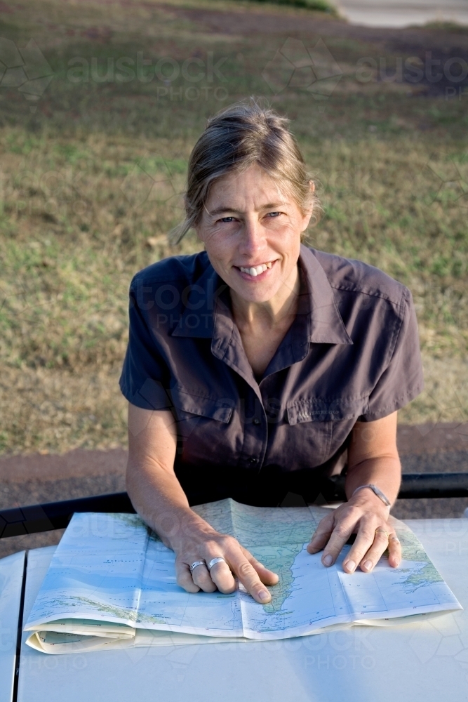 Woman leaning on bonnet of car with map, smiling at the camera - Australian Stock Image