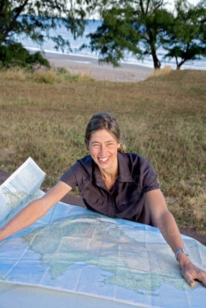 Woman leaning on bonnet of car with map, smiling - Australian Stock Image