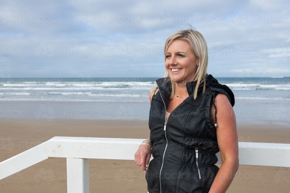 woman leaning on wooden railing at the beach - Australian Stock Image