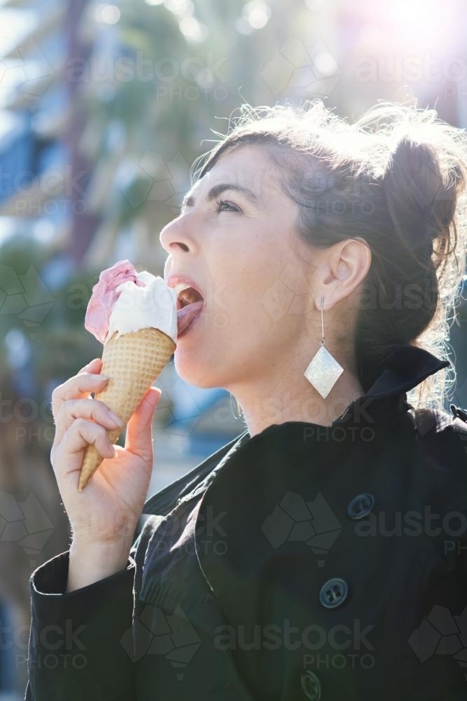 Woman licking an ice cream with sun flared behind - Australian Stock Image