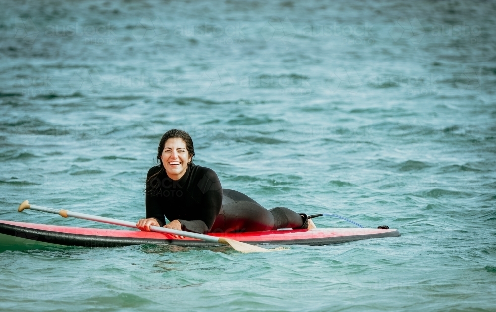 Woman lies on paddle board smiling. - Australian Stock Image