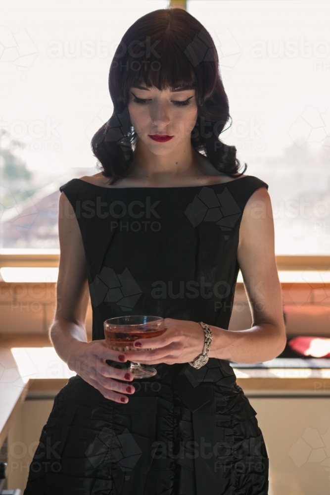 Woman looking at her glass of pink champagne in the kitchen - Australian Stock Image