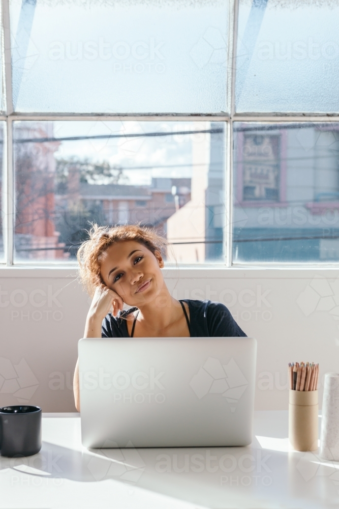 Woman looking content sitting behind her laptop in a beautiful studio : Austockphoto Woman looking content sitting behind her laptop in a beautiful studio - Australian Stock Image