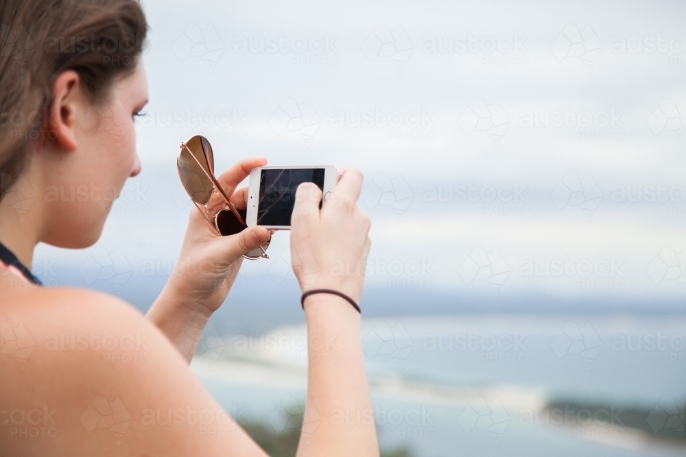 Woman looking out from Tomaree Head Summit walk taking photos of ocean and islands - Australian Stock Image