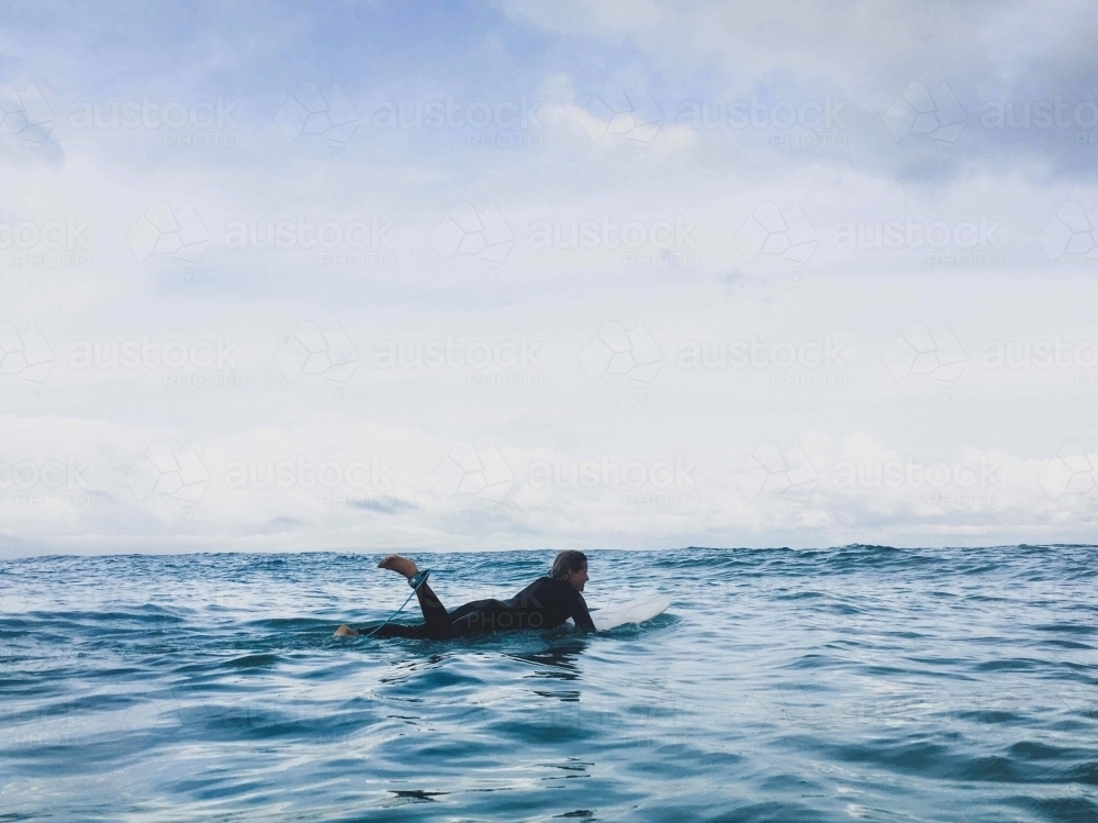 Woman lying on surfboard paddling out in ocean - Australian Stock Image