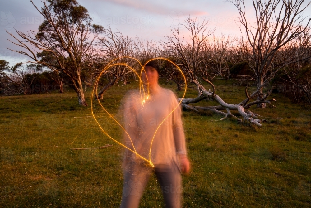 Woman making a heart shape with a sparkler at dusk - Australian Stock Image