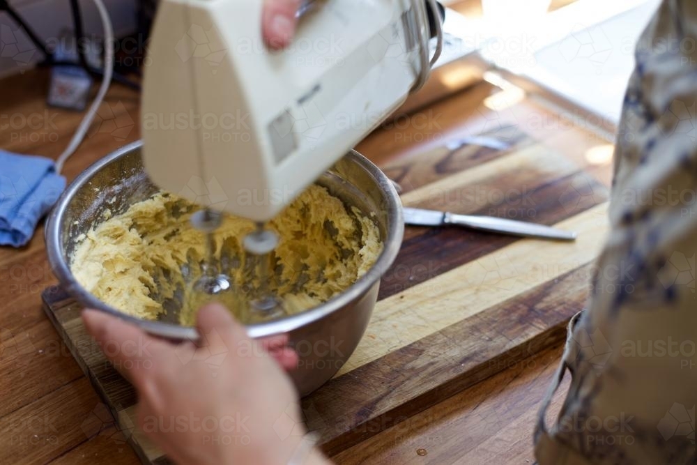 Woman making cake dough with an electric beater - Australian Stock Image