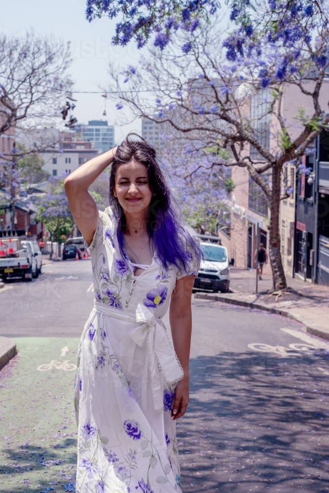 woman making fun face as she stands under jacaranda trees - Australian Stock Image