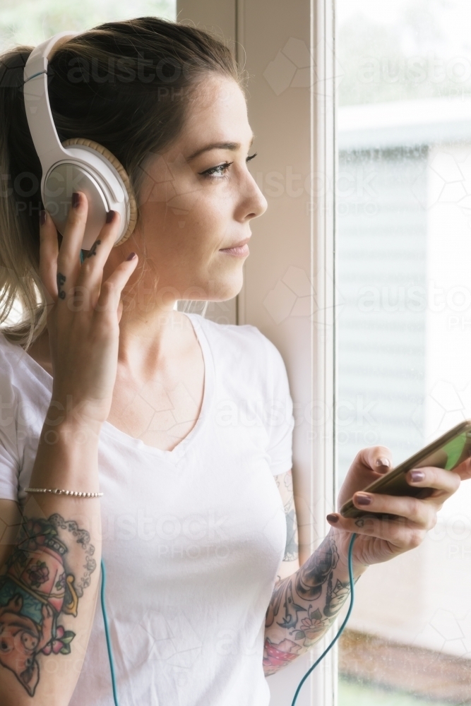 Woman playing music with her hand on her headphones looking away - Australian Stock Image