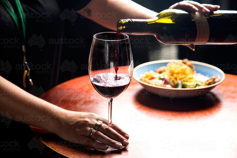 Woman pouring a glass of wine with meal in background - Australian Stock Image