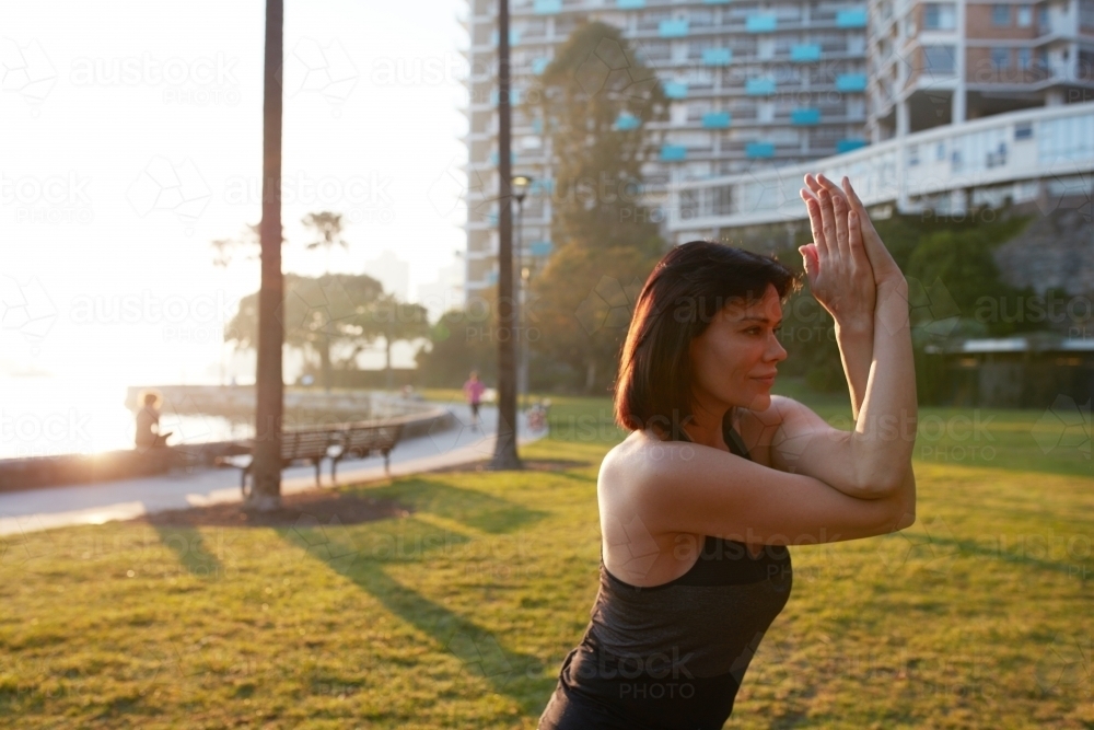 Image of Woman practising yoga at sunrise in the park by harbour ...
