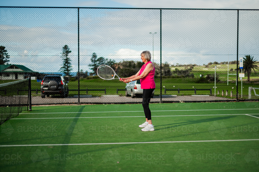 Woman prepares to hit a tennis ball on a green court surrounded by fencing in bright weather - Australian Stock Image