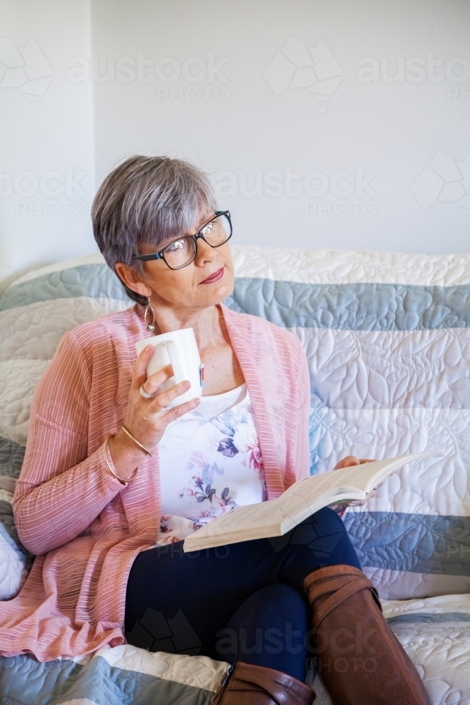 Woman reading a book on the lounge with cup of tea - Australian Stock Image