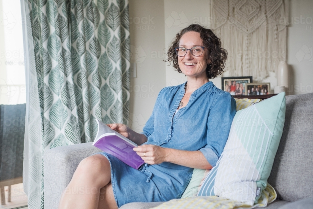 Woman reading book while seated on the couch - Australian Stock Image