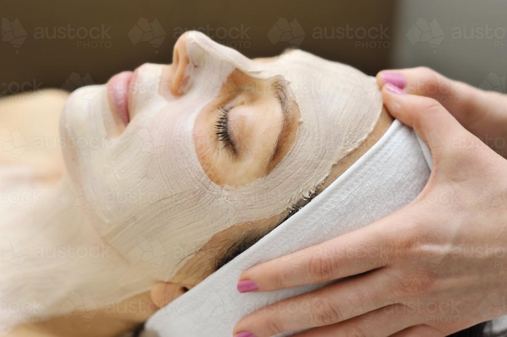 Woman relaxes as a beautician applies a fask mask during a beauty treatment - Australian Stock Image