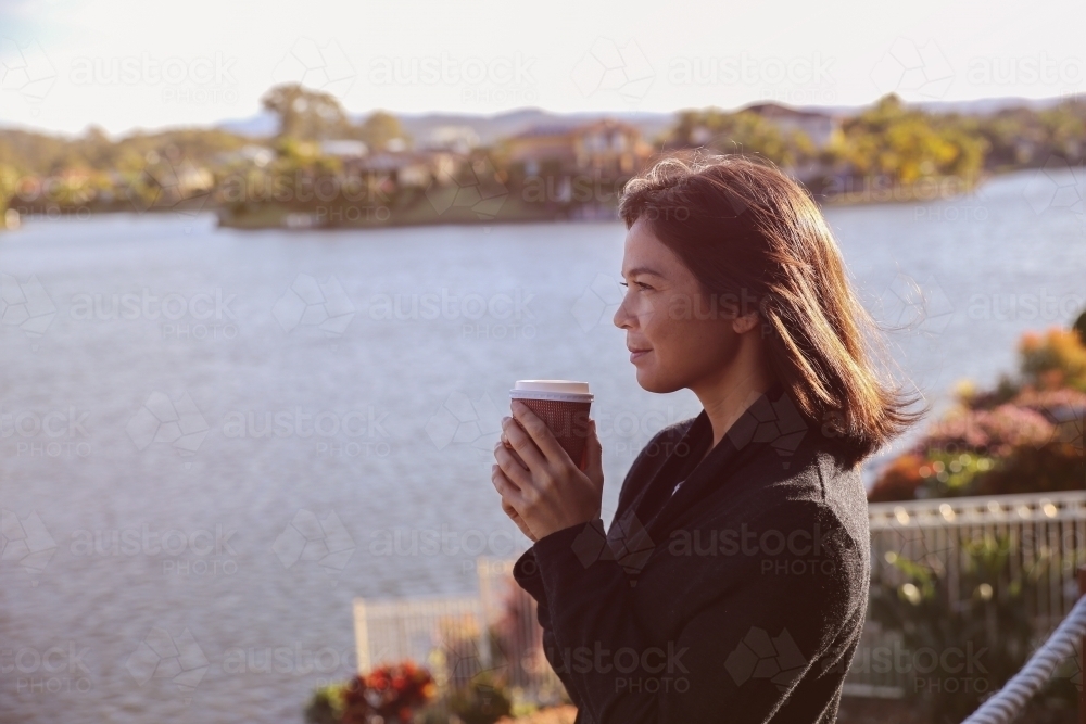 Woman relaxing and holding cup of coffee by the lake - Australian Stock Image