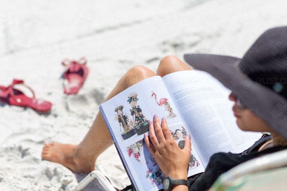 Woman relaxing and reading magazine on white sand beach - Australian Stock Image