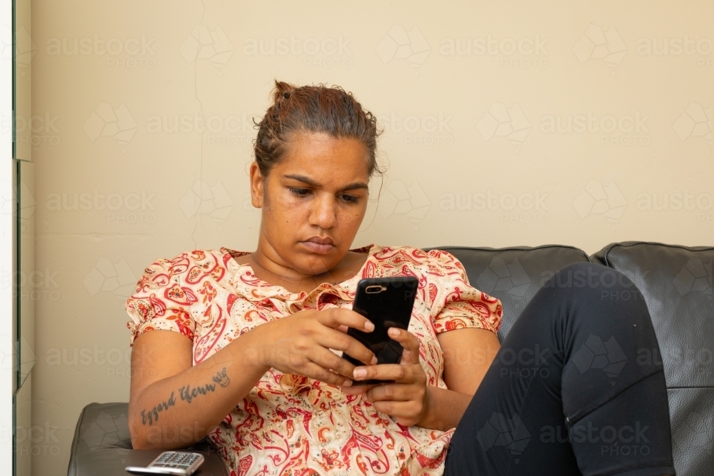 woman relaxing on sofa scrolling on smartphone - Australian Stock Image