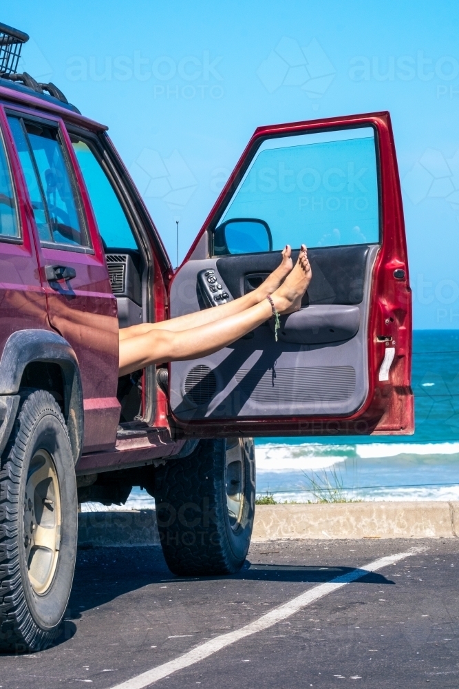 Woman rests legs in the car at a beach carpark - Australian Stock Image