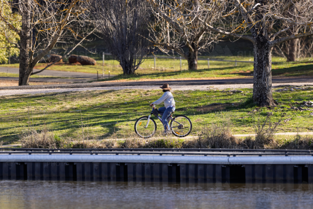 Woman riding bike on path beside lake - Australian Stock Image