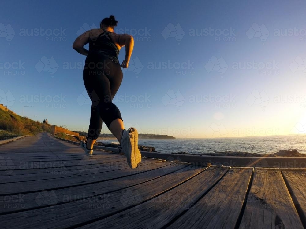 Woman running along ocean boardwalk at sunrise - Australian Stock Image
